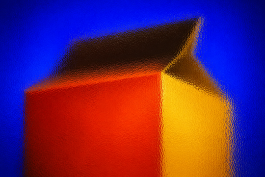 Unbranded folding carton seen through full-frame pebbled glass in ultramarine, vermilion and yellow light.