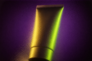 Unbranded squeeze tube seen through full-frame smoky rippled glass in aubergine, lime and gold light.