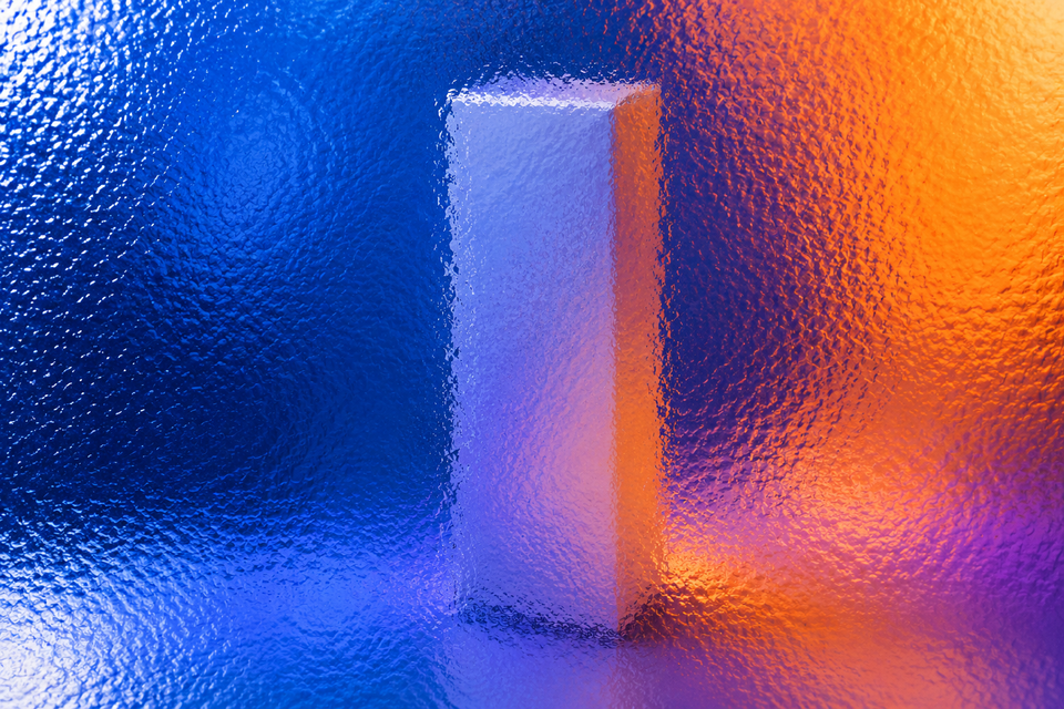 Unbranded slim skincare carton behind textured glass in vivid coloured light.