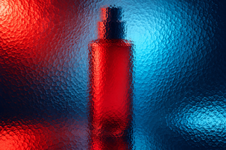 Unbranded tall cosmetic bottle behind textured glass in vivid coloured light.
