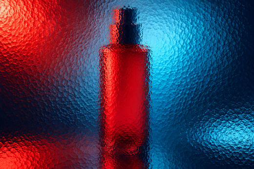 Unbranded tall cosmetic bottle behind textured glass in vivid coloured light.