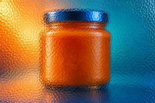 Unbranded wide condiment jar behind textured glass in vivid coloured light.