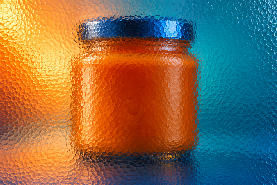 Unbranded wide condiment jar behind textured glass in vivid coloured light.
