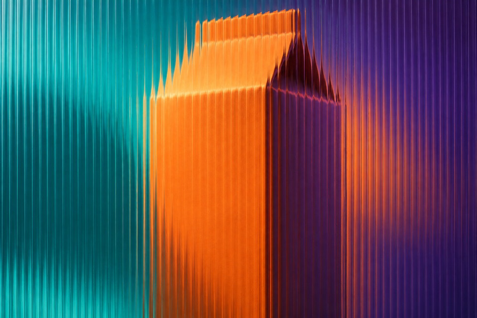 Unbranded orange food carton seen through full-frame fluted glass in teal, tangerine and deep-violet light.
