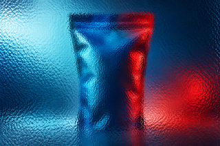 Unbranded tall snack pouch behind textured glass in vivid coloured light.