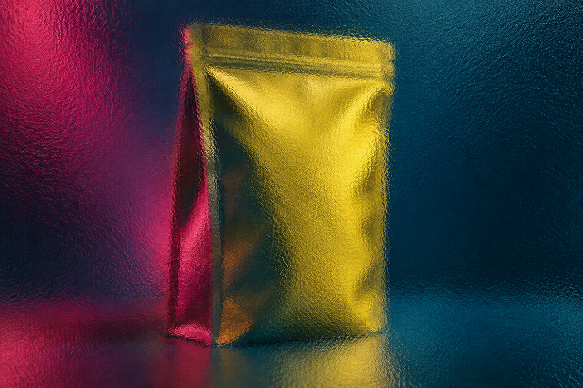 Unbranded yellow stand-up food pouch seen through full-frame pebbled glass in raspberry, yellow and deep petrol-blue light.