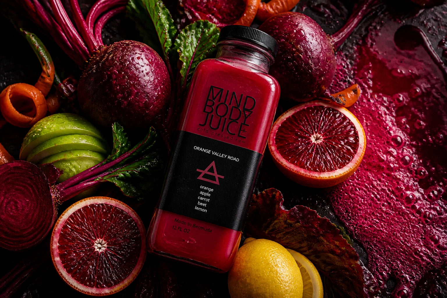 A bottle of Mind Body Juice orange-Valley Road smoothie placed on a dark surface surrounded by fresh ingredients including whole beets, sliced blood oranges, green apples, and lemons.