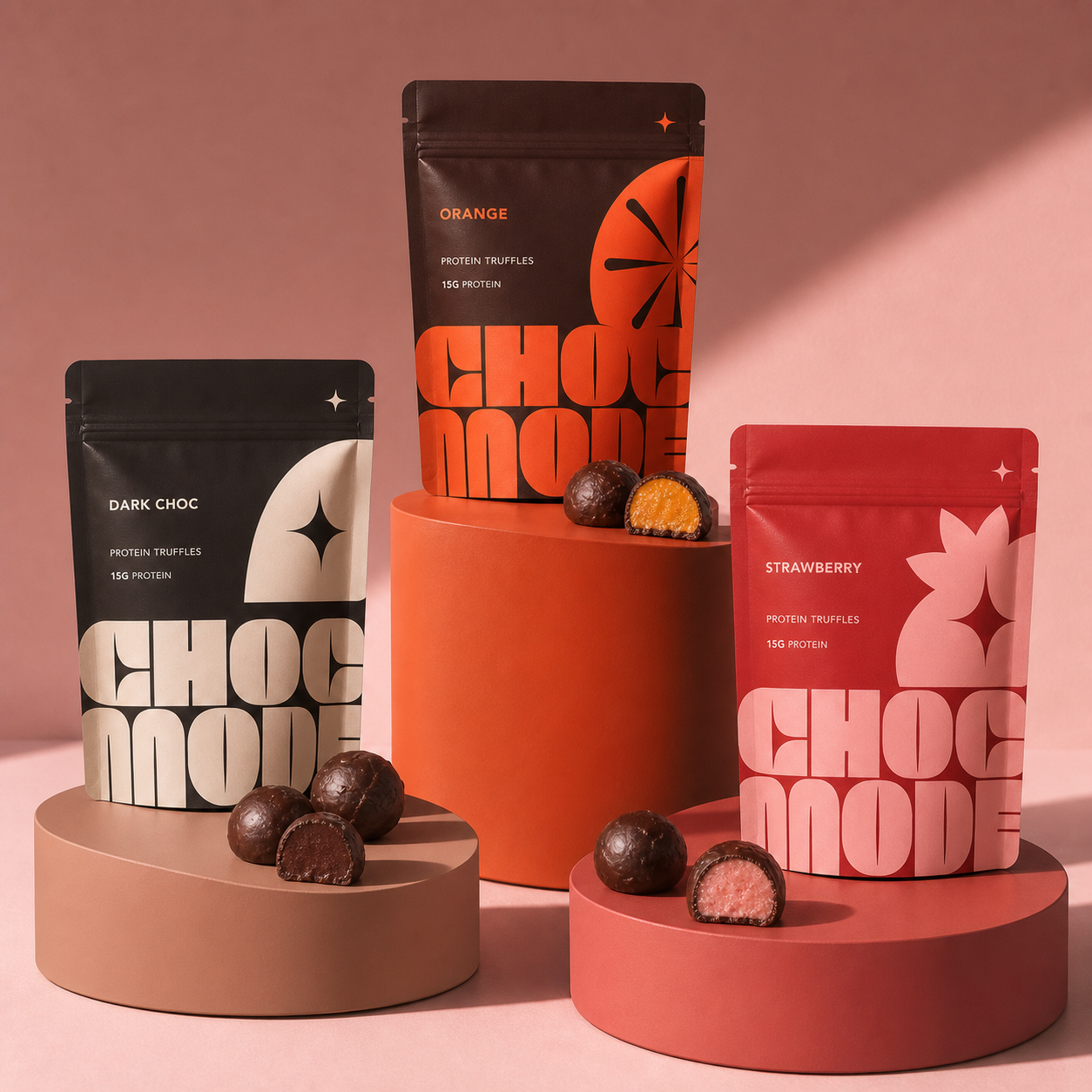 Dark chocolate, orange and strawberry CHOC MODE protein truffle pouches displayed on tonal circular pedestals with cut truffles.