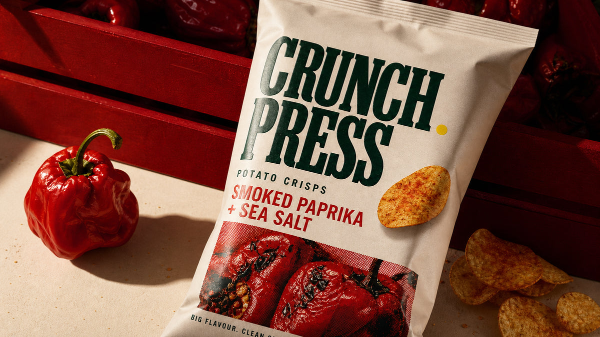 Close editorial crop of the Crunch Press crisp pouch with smoked peppers, loose crisps and bold green display typography.