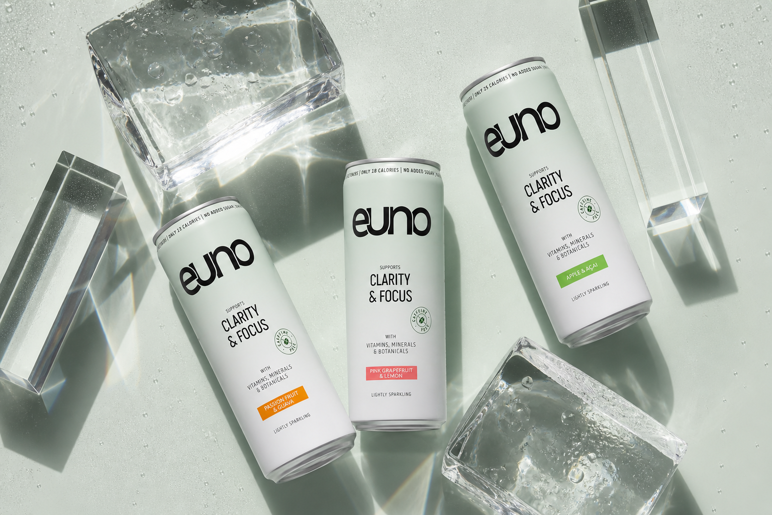 Overhead editorial still life of three Euno nootropic drink cans with clear ice, optical glass and cool mineral-green shadows