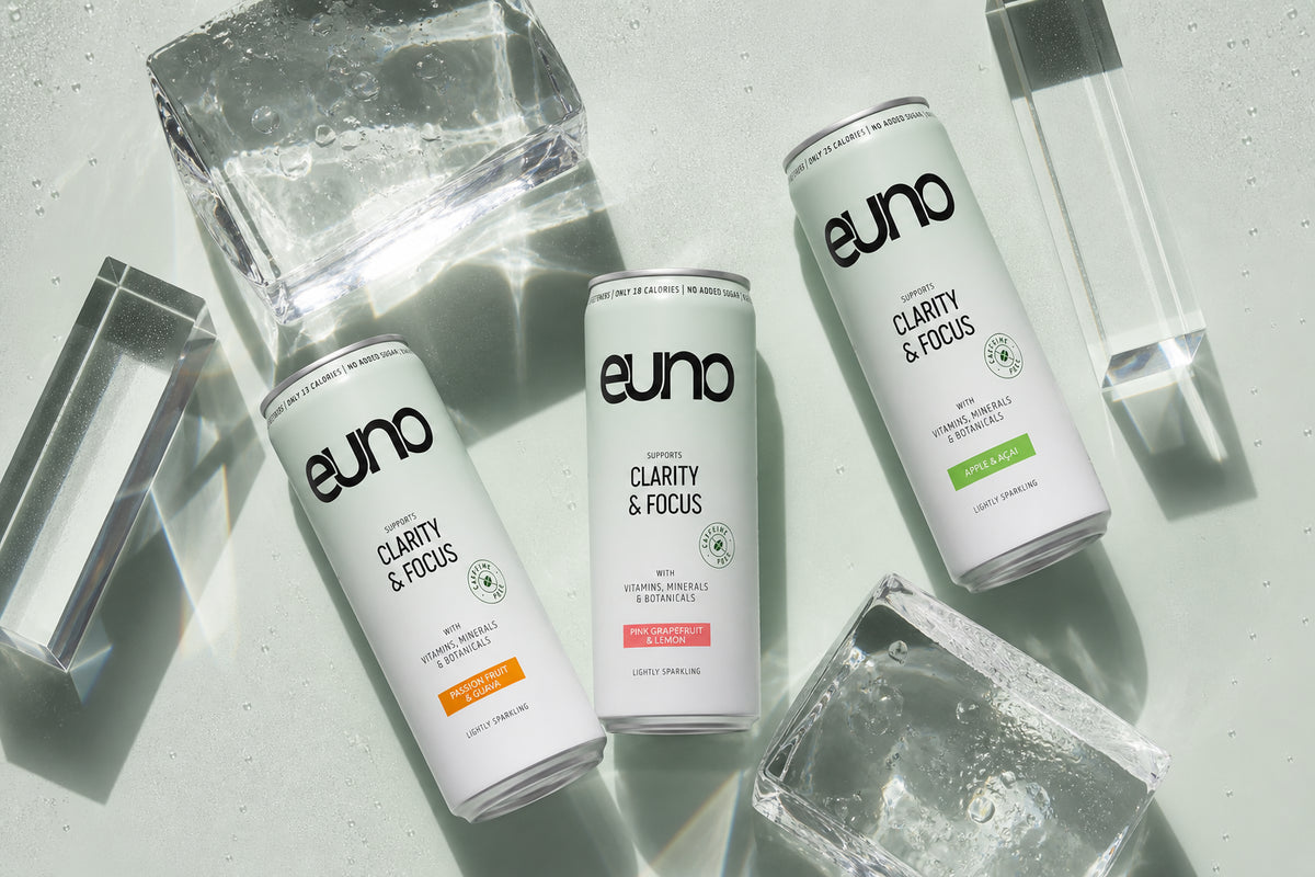 Overhead editorial still life of three Euno nootropic drink cans with clear ice, optical glass and cool mineral-green shadows