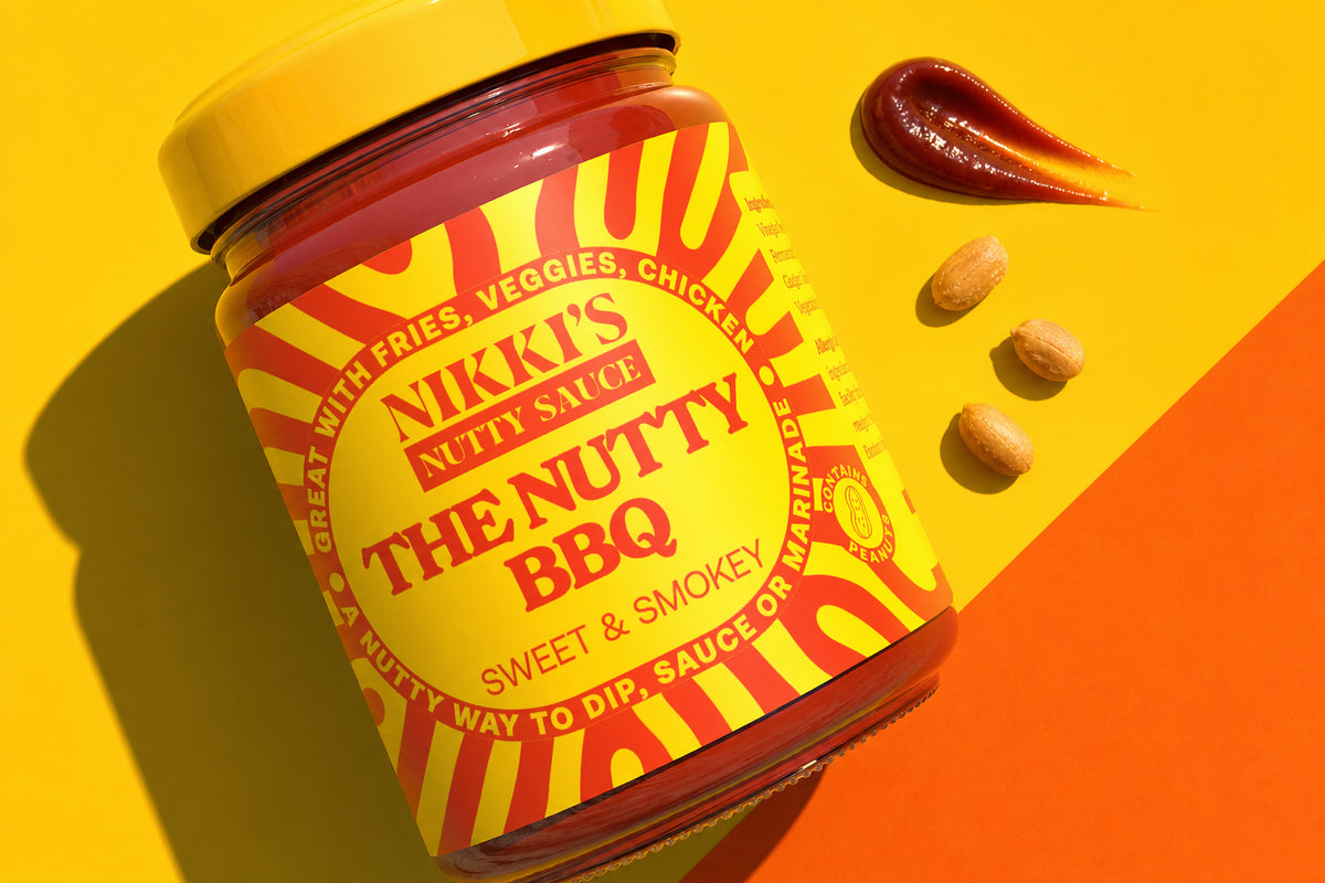 Nikki's Nutty BBQ sauce jar close-up with sauce and peanuts on a yellow studio set