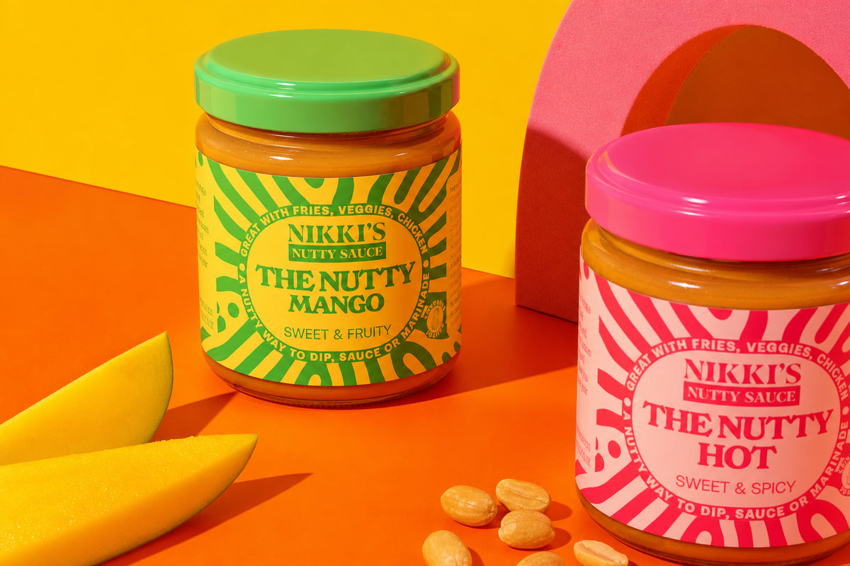 Nikki's Nutty Mango and Nutty Hot sauce jars with mango and peanuts in a colourful product still life