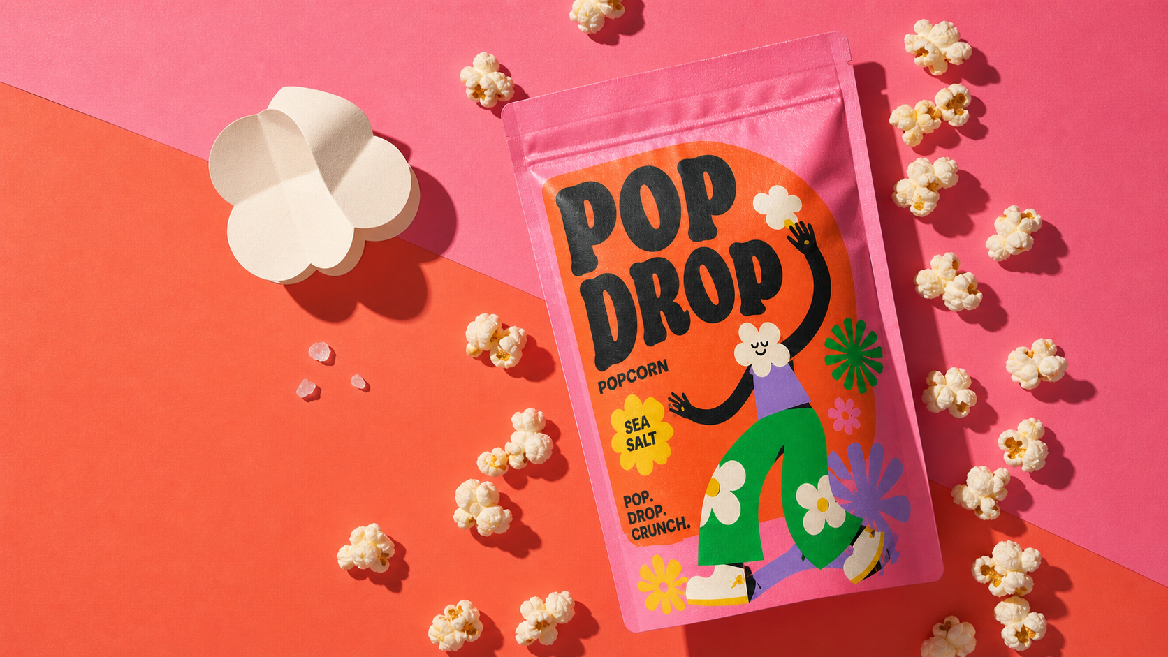 Overhead POP DROP Sea Salt popcorn packaging composition with loose popcorn and flower-shaped graphic props.