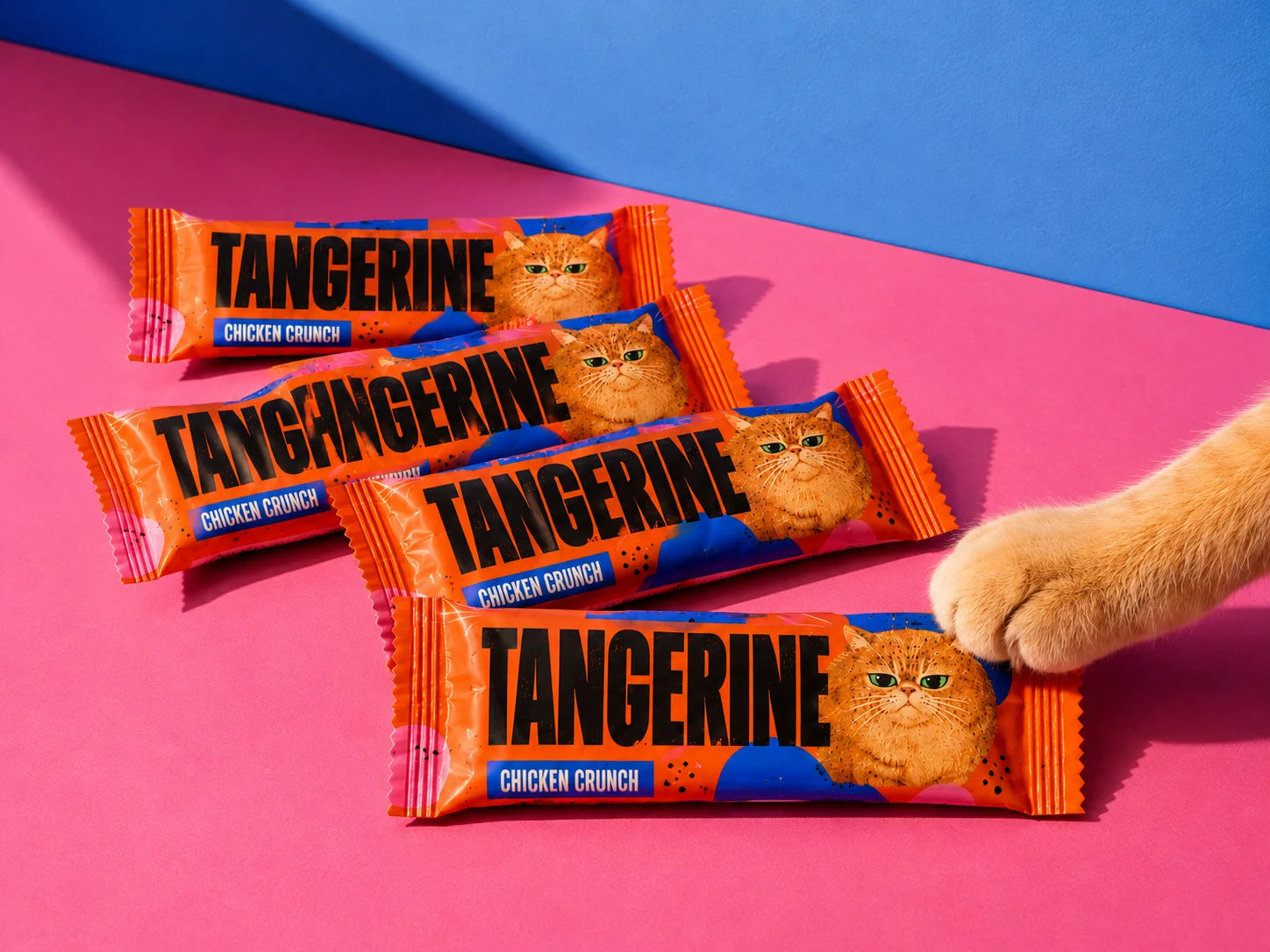 Tangerine Chicken Crunch cat treat sachet packaging arranged on a vivid pink and blue background